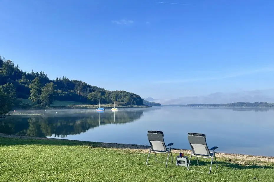 Blick von der Liegewiese von Camping Stein über zwei Liegestühle und den Simssee auf das Karwendelgebirge