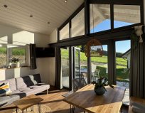 Chalet Leni - Wohnraum mit Sofa, Fernseher, Essbereich und Küche mit Kühlschrank, Spülmaschine und Mikrowelle